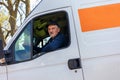 Cheerful delivery driver looking out the window of the white cargo van vehicle, delivering goods by car Royalty Free Stock Photo