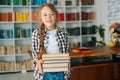 Portrait of cheerful elementary child school girl holding stack of books in library at school, looking at camera. Royalty Free Stock Photo