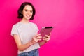 Portrait of cheerful excited freelancer using tablet searching news wearing white t-shirt isolated over pink fuchsia