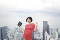 Portrait of cheerful excited pretty young female standing with skyscraper city view. Attractive woman in red dress holding digital Royalty Free Stock Photo