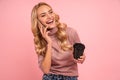 Portrait of a cheerful excited pretty young girl standing  over pink background, speaking by mobile phone and holding Royalty Free Stock Photo