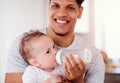 A portrait of father bottle feeding a small toddler son indoors at home.