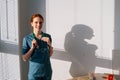 Portrait of cheerful female doctor in blue green uniform standing near window in sunny day in medical clinic office. Royalty Free Stock Photo