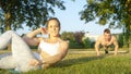 PORTRAIT: Cheerful girl does sit ups while happy boyfriend does push ups in park Royalty Free Stock Photo