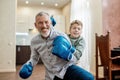 Portrait of a cheerful grandpa and little boy grandson wearing blue boxing gloves having fun and smiling at camera while Royalty Free Stock Photo