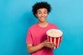 Portrait of cheerful guy with perming coiffure dressed stylish t-shirt hands hold pop corn basket isolated on blue color