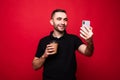 Portrait of a cheerful handsome young man standing isolated over red background, holding takeaway coffee cup, taking a selfie Royalty Free Stock Photo