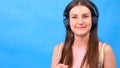 Portrait of a cheerful happy girl student with listening to music with headphones and dancing over a blue