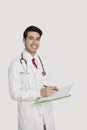 Portrait of a cheerful Indian male doctor holding a medical chart over light gray background Royalty Free Stock Photo