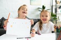 portrait of cheerful kids with drawing at table with pencils