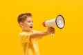 Portrait of cheerful little boy, child in bright T-shirt shouting in megaphone, posing isolated over yellow background Royalty Free Stock Photo