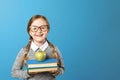 Portrait of a cheerful little girl with glasses on a blue background. Schoolgirl is holding a stack of books and an apple. Royalty Free Stock Photo