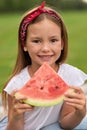 Portrait of cheerful little girl looking at camera while holding watermelon slice, family having a picnic in the green Royalty Free Stock Photo