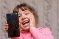 Portrait of a cheerful little girl with a mobile phone. The child broke the telephone communicator and laughs. Baby joked breaking Royalty Free Stock Photo