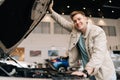 Portrait of cheerful male customer checking at engine compartment at car dealership, smiling looking at camera. Happy