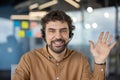 Portrait of a cheerful male customer service representative wearing a headset and waving in a modern office setting. Royalty Free Stock Photo