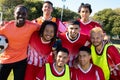 Portrait of cheerful male soccer team players wearing uniforms with arms around posing in playground