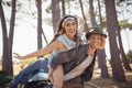 Portrait of cheerful man piggybacking woman against trees