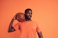 Portrait of a cheerful man wearing an orange t-shirt holding basket ball on his shoulder Royalty Free Stock Photo