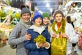 Portrait of man and woman and their happy teenagers posing with paper bags near counters at Christmas fair