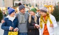 Portrait of man and woman and their happy teenagers posing with paper bags near counters at Christmas fair