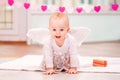 Portrait of cheerful mischievous baby with white angel wings crawling towards viewer