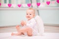 Portrait of a cheerful mischievous baby with white angel wings sitting against background of garland of hearts on a terry towel Royalty Free Stock Photo