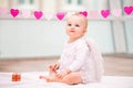 Portrait of a cheerful mischievous baby with white angel wings sitting against background of garland of hearts on a terry towel Royalty Free Stock Photo