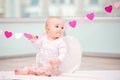 Portrait of cheerful mischievous baby with white angel wings touching heart ornament Royalty Free Stock Photo