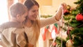 Portrait of cheerful young mother with little boy decorating Christmas tree with colorful ribbons Royalty Free Stock Photo