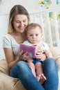 Portrait of cheerful mother reading book to her baby boy at living room Royalty Free Stock Photo