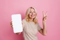 Portrait of cheerful nice person demonstrate v-sign empty space smart phone screen offer isolated on pink color