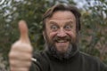 Portrait of cheerful optimist senior man looking at camera with thum up. Elderly bearded caucasian male in outdoor in urban park