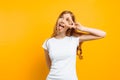 Portrait of a cheerful girl showing two fingers with winking eyes showing tongue against yellow background Royalty Free Stock Photo