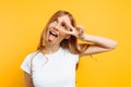 Portrait of a cheerful girl showing two fingers with winking eyes showing tongue against yellow background Royalty Free Stock Photo
