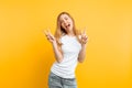 Portrait of a cheerful girl showing two fingers with winking eyes showing tongue against yellow background Royalty Free Stock Photo