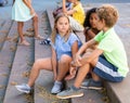 Cheerful preteen girls and boys sitting on steps outdoors and chatting