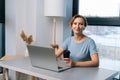 Portrait of cheerful pretty blonde woman working on laptop computer, holding cup with coffee, looking at camera, sitting Royalty Free Stock Photo