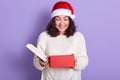 Portrait of cheerful pretty brunette waiting for Christmas, holding red box in hands, opening it, getting presents, looking inside