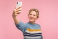 Portrait of cheerful pretty woman with short curly hair in warm sweater smiling and doing selfie using cellphone Royalty Free Stock Photo