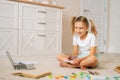 Portrait of cheerful primary girl child writing homework in notebook sitting on floor at home, looking at camera. Royalty Free Stock Photo