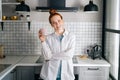 Portrait of cheerful redhead woman holding cup of hot beverage in hands on morning at kitchen. Royalty Free Stock Photo