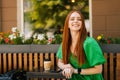 Portrait of cheerful redhead young woman sitting at table with coffee cup and mobile phone in outdoor cafe terrace in Royalty Free Stock Photo