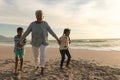 Portrait of cheerful senior biracial woman holding hands with grandchildren while walking at beach