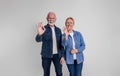 Portrait of cheerful senior couple showing OK signs while standing confidently on white background