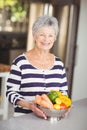 Portrait of cheerful senior woman holding colander with vegetables