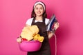 Portrait of cheerful sincere housewife looking directly at camera, wearing brown apron, white headband and t shirt, holding pink Royalty Free Stock Photo