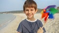 Portrait of cheerful smiling boy having fun on sea beach with colorful pinwheel. Concept of summer holiday, happiness, joy, travel Royalty Free Stock Photo