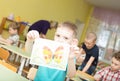 Portrait of cheerful smiling boy holding a bright colorful picture of butterfly painted colors and crayons in kindergarten -