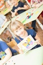 Portrait of cheerful smiling girl holding a bright colorful picture of butterfly painted colors and crayons in kindergarten -